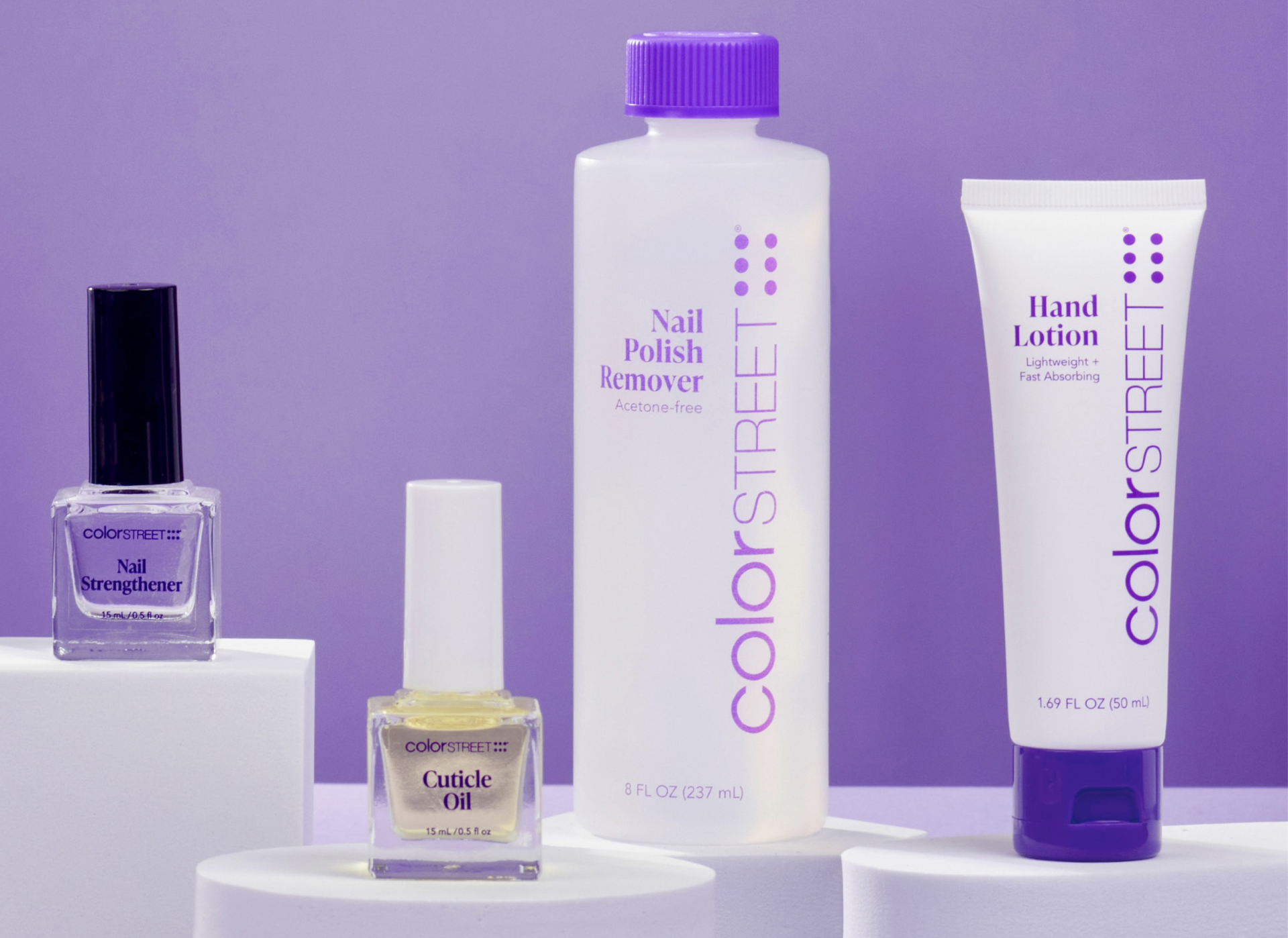 Color Street Nail Care products on white pedestals. Includes Nail Strengthener in a glass bottle with a black lid/handle; cuticle oil in a glass bottle with a white lid/handle, acetone free nail polish remover in a plastic bottle with purple lid; hand lotion in a white tube with purple cap.